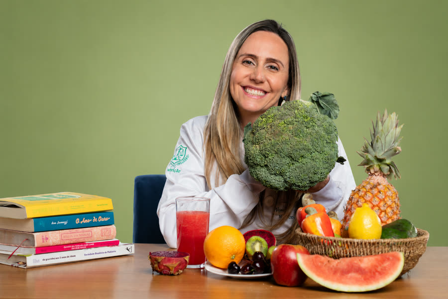 Vanessa Neiva, nutricionista materno-infantil, segurando um brócolis ao lado de frutas frescas